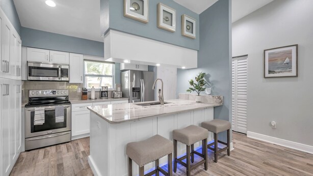 Una cocina moderna con armarios blancos, electrodomésticos de acero inoxidable y una isla central con taburetes.
