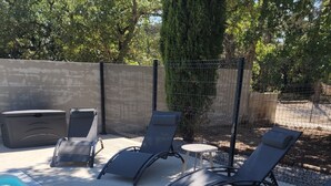 A swimming pool with lounge chairs and a small table, surrounded by a fence and trees.