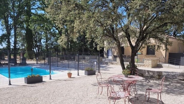 A pool area with a fenced pool, outdoor seating, and trees.