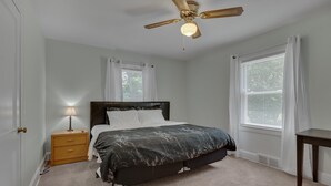 A bedroom with a bed, a nightstand, a ceiling fan, and two windows with curtains. - Duke East Campus 2BR Buchanan (Durham)