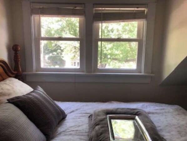 A bedroom with a bed, pillows, and a window with a view of greenery.