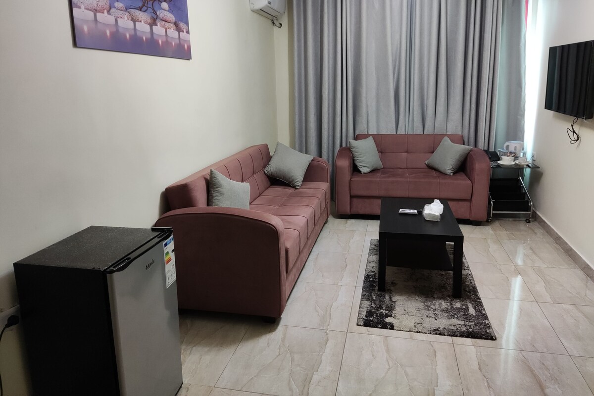 Una sala de estar con dos sofás, una mesa de centro, un televisor y un refrigerador pequeño.