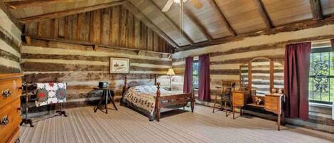 Een slaapkamer in een blokhut, met een bed, een houten dressoir en een plafondventilator.