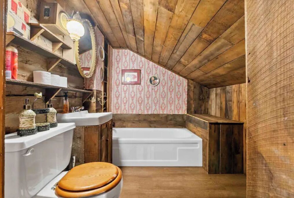 A rustic bathroom with wooden walls, a white bathtub, and a wooden toilet.
