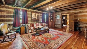A cozy log cabin interior with a wooden floor, a patterned rug, a rocking chair, a sofa, and a bookshelf. - Spacious Large Cabin at Harding near I-65/Downtown Franklin (Franklin)