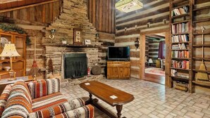 A rustic log cabin interior with a fireplace, television, sofa, and bookshelf. - Spacious Large Cabin at Harding near I-65/Downtown Franklin (Franklin)