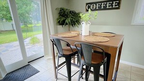 Un espace repas comprenant une table, des chaises, un panneau indiquant qu'on y sert du café et une plante.
