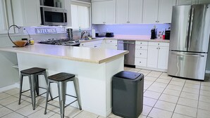 Une cuisine moderne avec des meubles blancs, des appareils en acier inoxydable, un grand îlot central doté de tabourets et une poubelle.