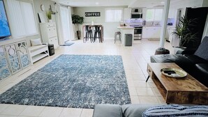 Un salon moderne avec un tapis bleu, un canapé, une table basse et un coin cuisine à l’arrière-plan.