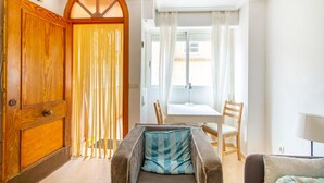 A room with a wooden door, a window with curtains, a table with chairs, and a sofa with a cushion. - Beach front home in Santa Pola (Santa Pola)