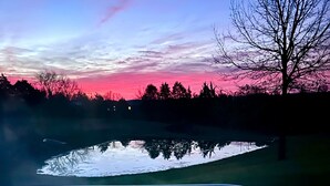 A hot tub with a digital thermometer reading 104°F, surrounded by a serene landscape with a reflective pond and trees against a sunset sky. - Barndominium on the Bourbon Trail - Hot Tub and Horses!  Dog and Horse friendly! (Lawrenceburg)