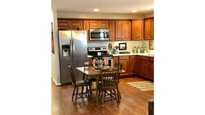A kitchen with wooden cabinets, a stainless steel refrigerator, a microwave, and a stove. There is a dining table with chairs and a rug on the floor. - Barndominium on the Bourbon Trail - Hot Tub and Horses!  Dog and Horse friendly! (Lawrenceburg)