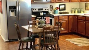 A kitchen with wooden cabinets, a stainless steel refrigerator, a microwave, and a stove. There is a dining table with chairs and a rug on the floor.