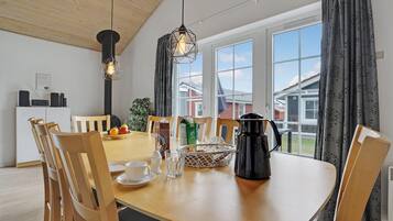 A dining area with a wooden table, chairs, a coffee maker, and a fruit bowl.