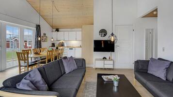 En moderne stue med en grå sofa, et sofabord og et spiseområde med træstole og et bord.
