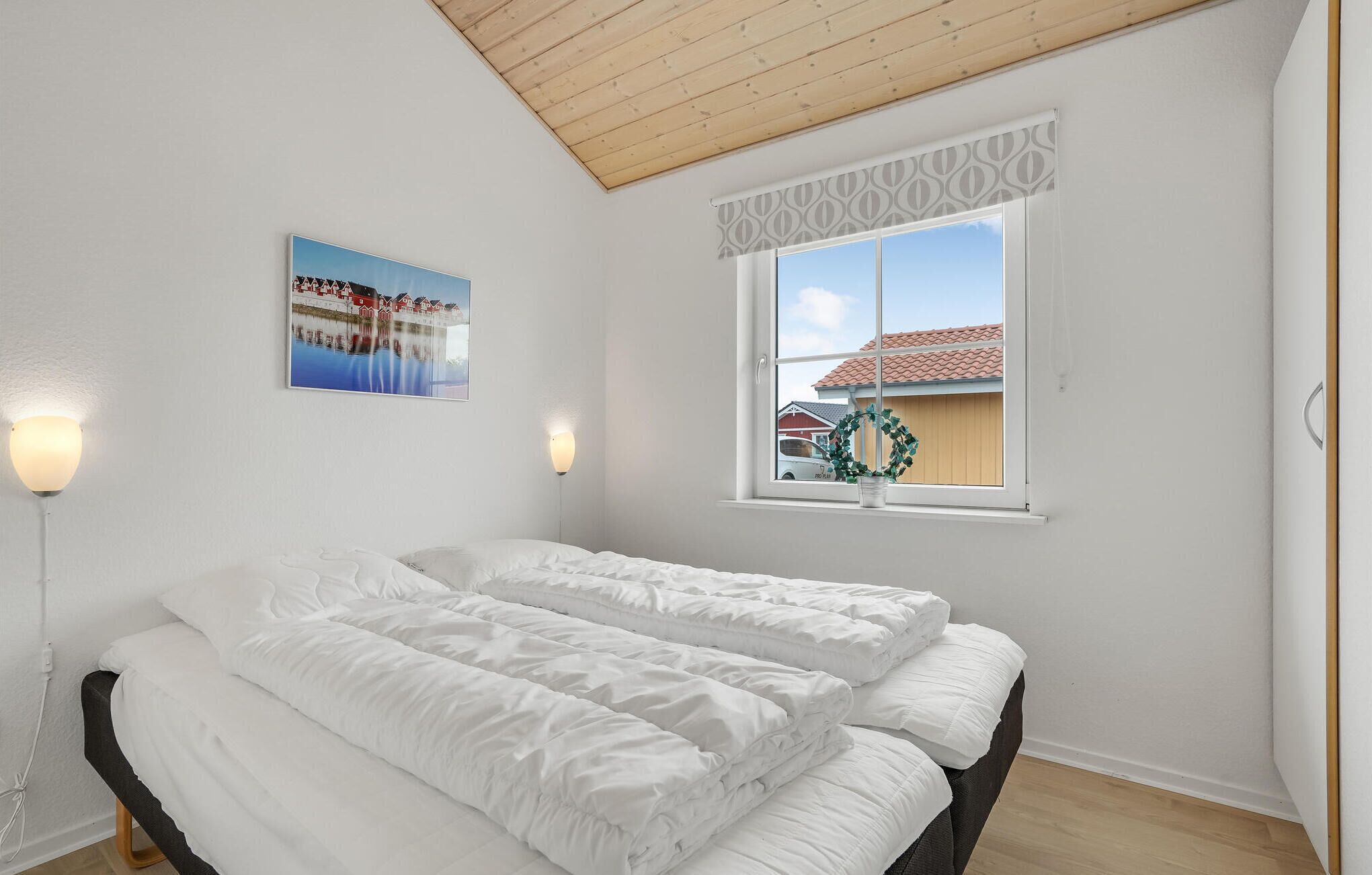 A bedroom with a bed, a window with a view of houses, and a wall-mounted picture.