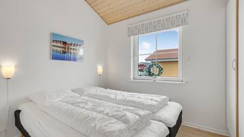 A bedroom with a bed, a window with a view of houses, and a wall-mounted picture.