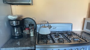 Et køkken med gaskomfur, kaffemaskine og diverse køkkenredskaber.