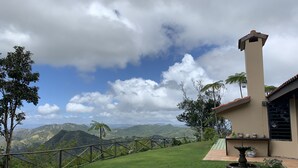 Ein Haus mit Bergblick, einem eingezäunten Rasen und einem Springbrunnen.
