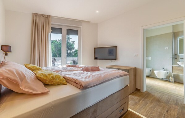 A bedroom with a bed, a TV, a window with curtains, and a bathroom visible through an open door. - Gorgeous home in Porec (Porec)