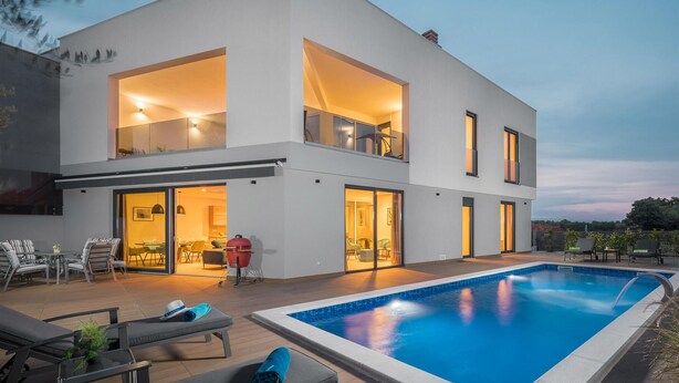 Une maison moderne à deux étages, dotée d’une piscine, de grandes fenêtres et d’un espace de vie à aire ouverte.