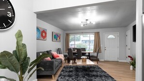 Un salon moderne avec un canapé gris, un tapis noir et un coin repas comprenant une table et des chaises.