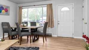 Un coin repas avec une table en bois et quatre chaises rembourrées, une fenêtre avec des rideaux et une porte blanche.