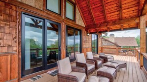 A covered outdoor deck with wicker furniture and large windows. - Lucky 7 at Eagles Nest: Long Range Views | Huge Deck | Firepit | Walk to Tennis! (Banner Elk)