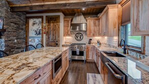 A kitchen with wooden cabinets, a stone wall, and a large island with a marble countertop. - Lucky 7 at Eagles Nest: Long Range Views | Huge Deck | Firepit | Walk to Tennis! (Banner Elk)