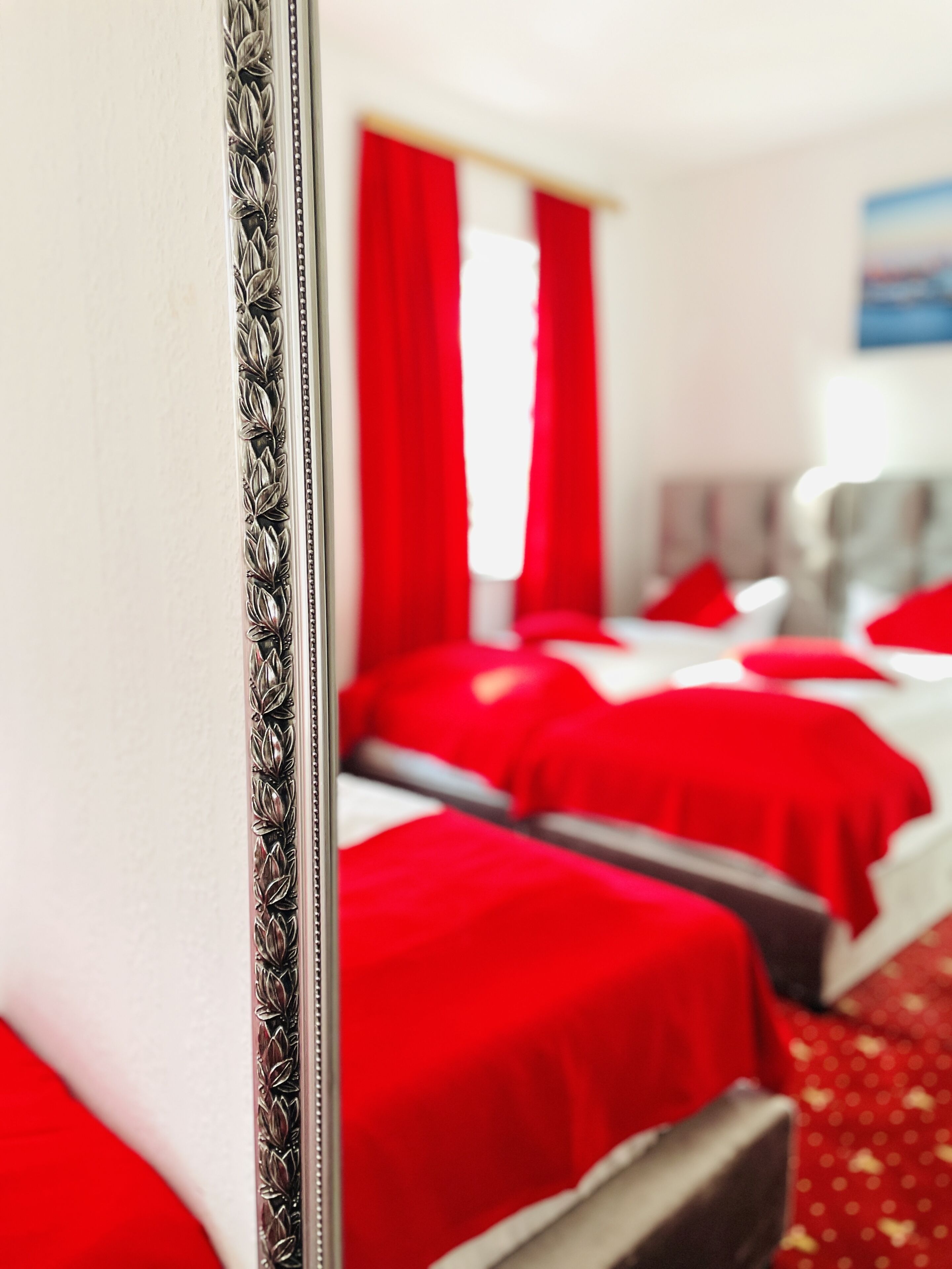 Ein Hotelzimmer mit einem großen Spiegel, roten Vorhängen und mehreren Betten mit roter Bettwäsche.
