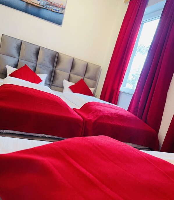 Una habitación de hotel con cama, ropa de cama roja y cabecera gris.