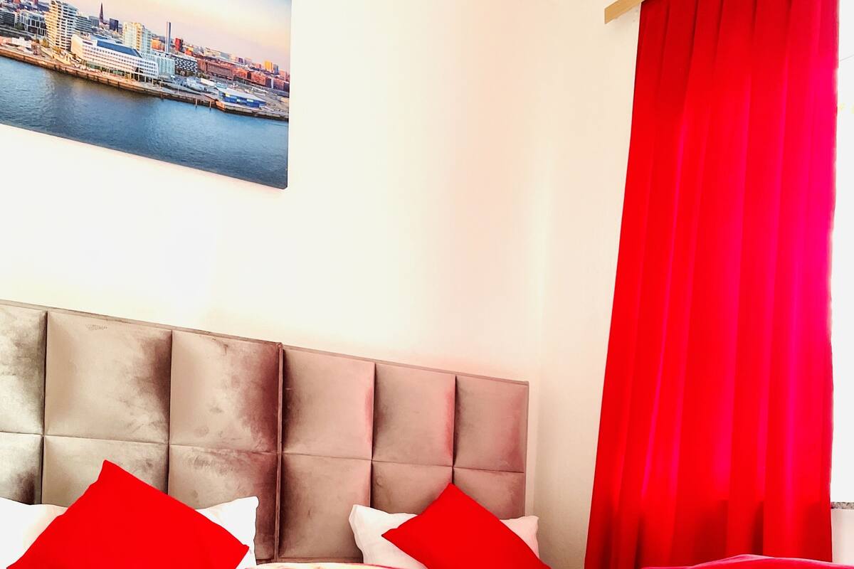 A hotel room with a large bed, red bedding, and a cityscape view.