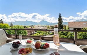 A table with a glass of water, a glass of wine, and a bowl of fruit on a balcony with a mountain view. - Awesome apartment in Füssen Hopfen am See (Füssen Hopfen am See)