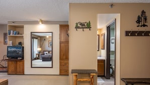 Un espacio habitable pequeño con televisor, muebles de madera, un espejo y un perchero.