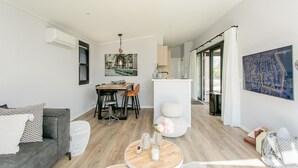 Ein modernes Wohnzimmer mit grauem Sofa, einem Essbereich mit Holztisch und einer Küche mit weißer Arbeitsplatte.