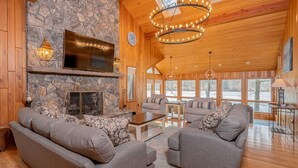 A cozy living room with a stone fireplace, wooden ceiling, and large windows. - Gone Fish Inn by Taylor Made Deep Creek (McHenry)