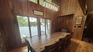 A wooden dining area with a large table and chairs, large windows with a view of a lake, and a sign that reads "Live a Good Life". - Gone Fish Inn by Taylor Made Deep Creek (McHenry)