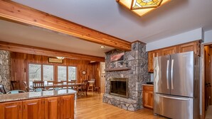 A spacious kitchen with wooden cabinets, a stone fireplace, and a stainless steel refrigerator. - Gone Fish Inn by Taylor Made Deep Creek (McHenry)