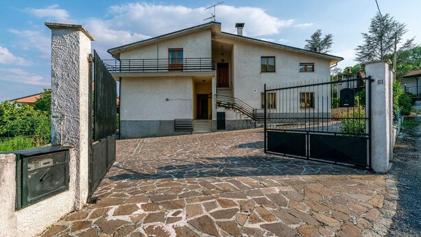 Ein zweistöckiges Haus mit einem gepflasterten Eingangsbereich und einem Metallgitter.