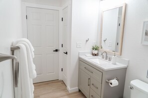 Un baño con puerta blanca, un lavamanos con espejo y un inodoro.