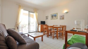 Ein Wohnzimmer mit einer Couch, einem Couchtisch, einem Esstisch mit Stühlen, einem Fernseher und einem Fenster mit Vorhängen.