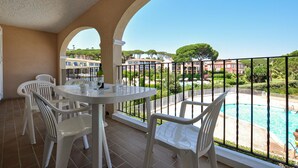 Ein Balkon mit Blick auf einen Pool, weißen Stühlen und einem Tisch mit Flasche und Gläsern.