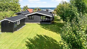 Moderni, kaksikerroksinen talo, jossa on tumma julkisivu, hyvin hoidettu nurmikko ja näkymä merelle.