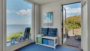 Una habitació acollidora amb una banca, vista al mar i una porta que dona a l'exterior.