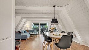 A modern loft with a dining area featuring a round table and black chairs, a grey sofa, and a hanging black pendant light. - 2 bedroom cozy home in Farsø (Farsø)