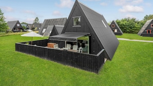 A modern, black-roofed building with a sloped roof and a covered outdoor seating area with chairs and a table. - 2 bedroom cozy home in Farsø (Farsø)