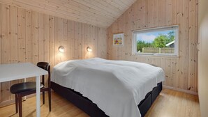 A bedroom with a wooden paneled ceiling and walls, a bed with white bedding, a small table with a chair, and a window with a view of greenery. - Gorgeous home in Rødby with WiFi (Rødby)