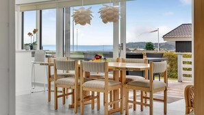 Een eetruimte met houten stoelen en een tafel, grote ramen met uitzicht op de zee, en hangende吊り灯.