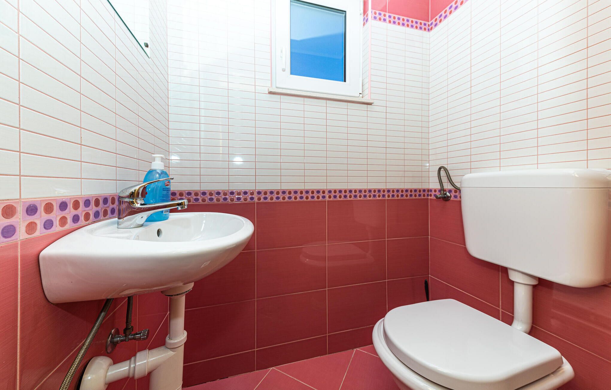 Ein Badezimmer mit einem weißen Waschbecken, einer Toilette und einem Fenster über dem Waschbecken.