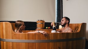 Deux personnes dans une baignoire en bois, avec une bouteille de champagne et un verre.